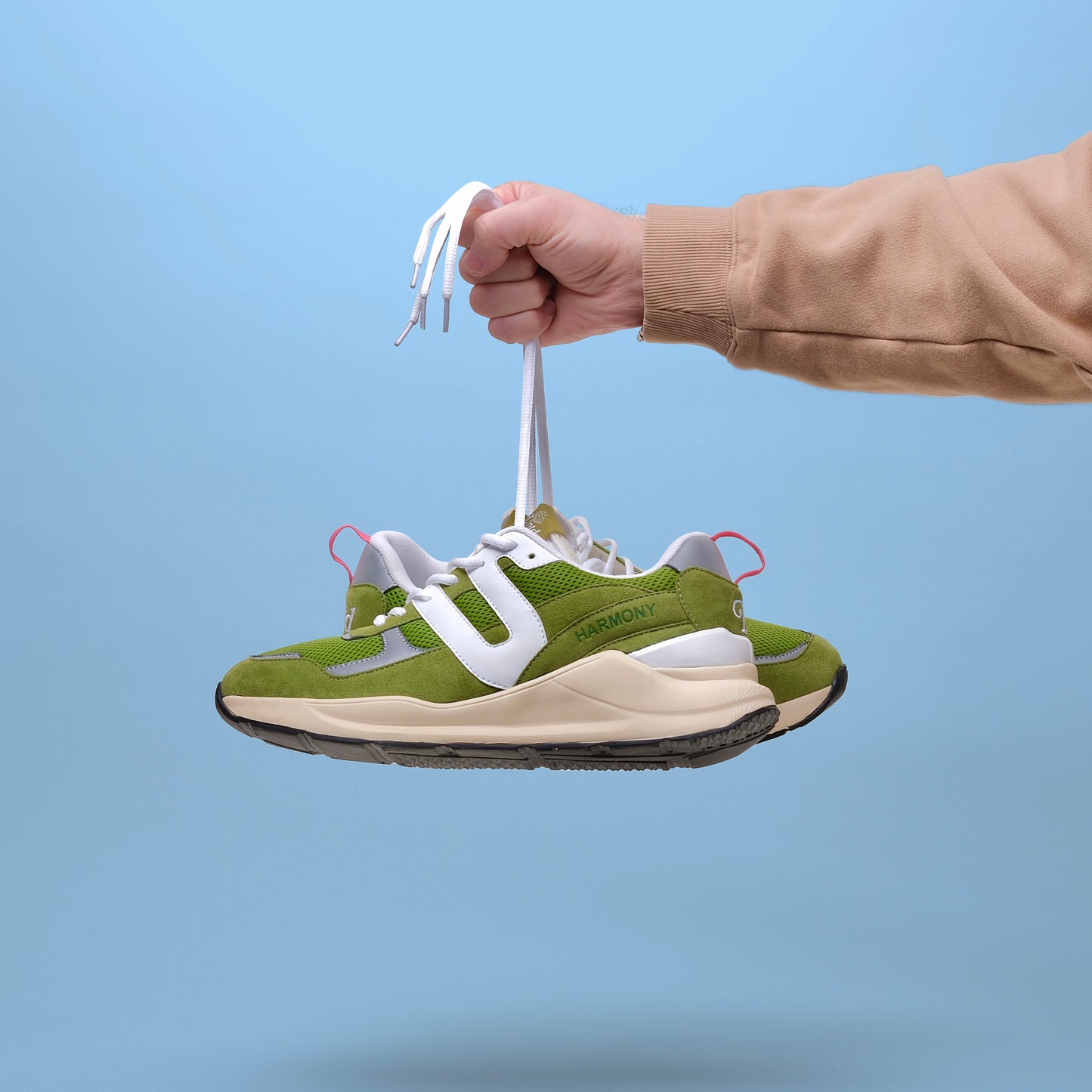 Two UNTD Harmony Runner "Matcha" sneakers, green and white with suede and mesh details, on a blue background